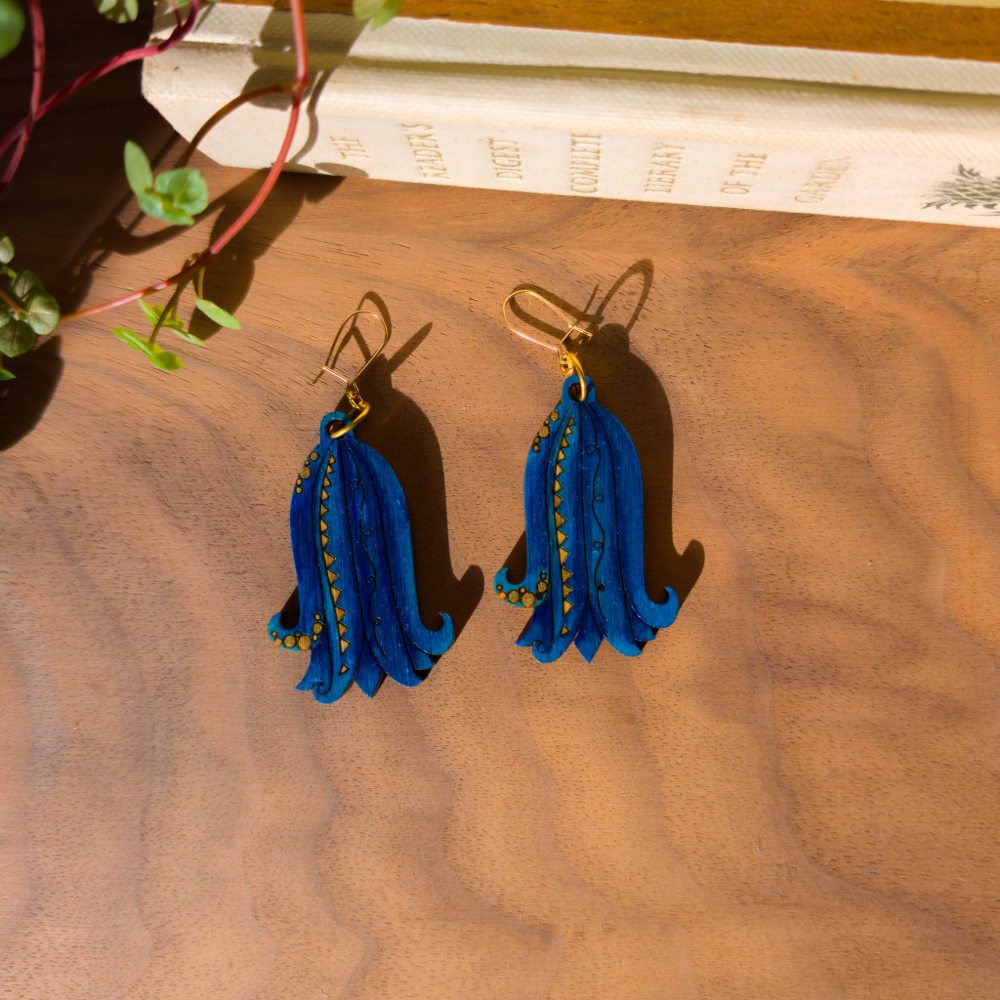 A pair of bluebell earrings laying on a wooden background, showing the laser etched detail.