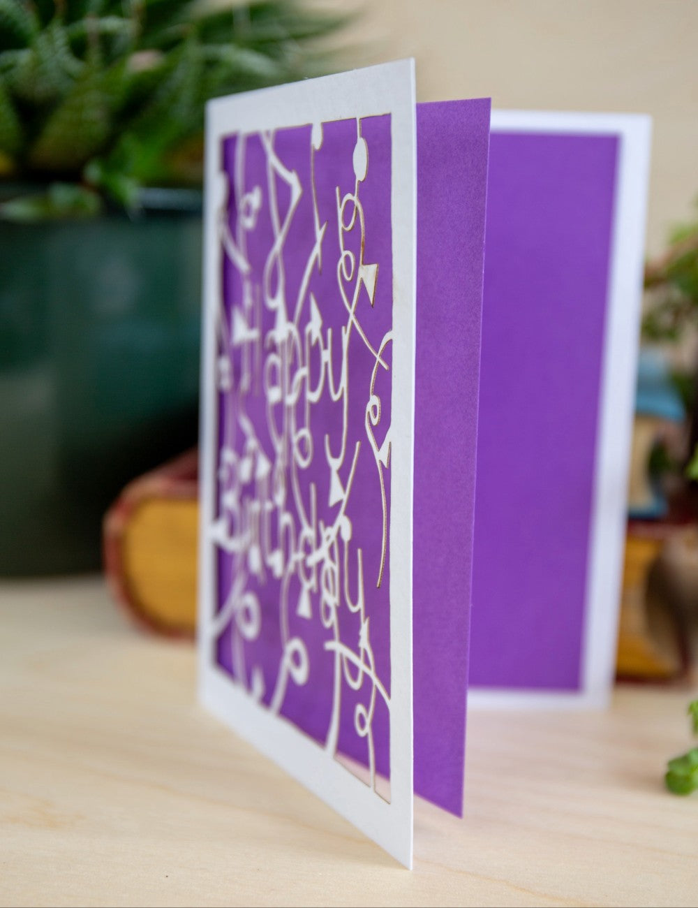 Side view of open laser cut happy birthday card with a bright purple insert. Showing the layers and detail of the card.