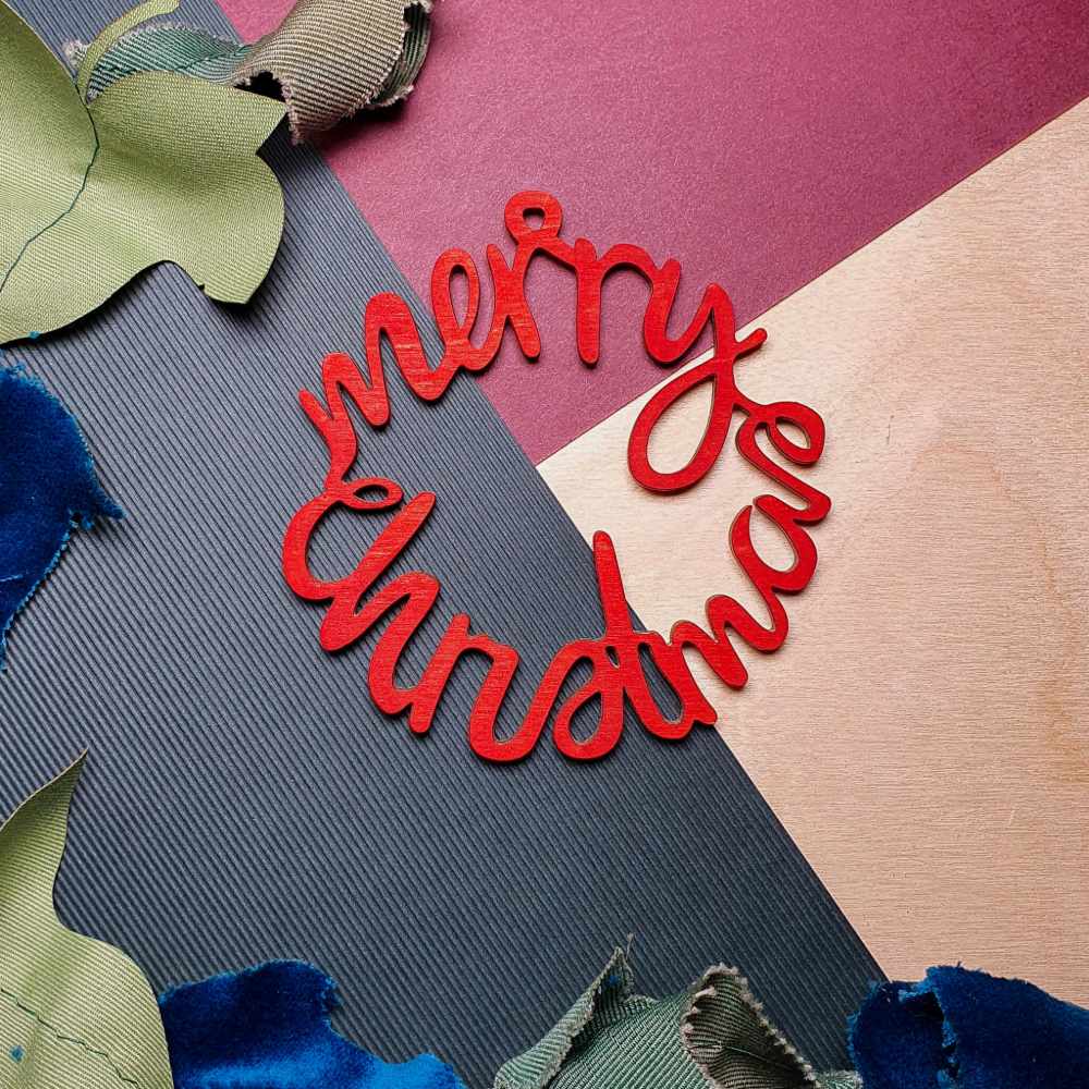 A hand-painted, red 'Merry Christmas' decoration laid on a surface with varied colors and textures.