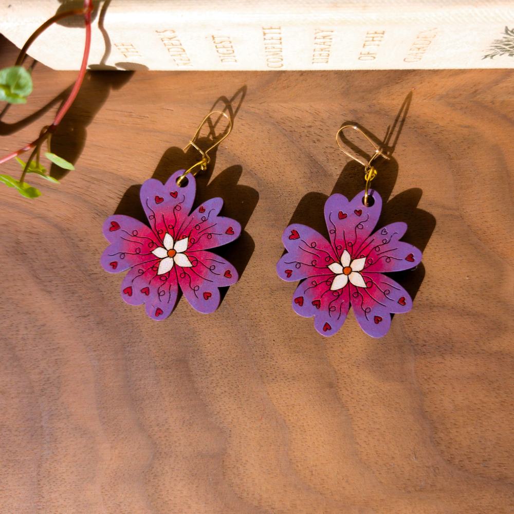 Wooden primrose shaped earrings with laser cut engraved details. Hand painted in pink and purple with red heart and white details.