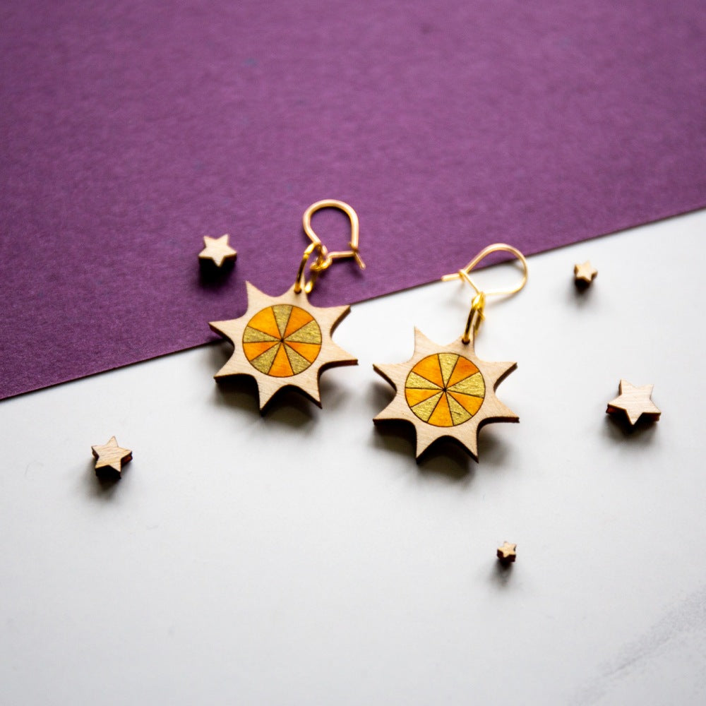 Laser cut and hand painted sun earrings in gold and yellow on a white and purple background