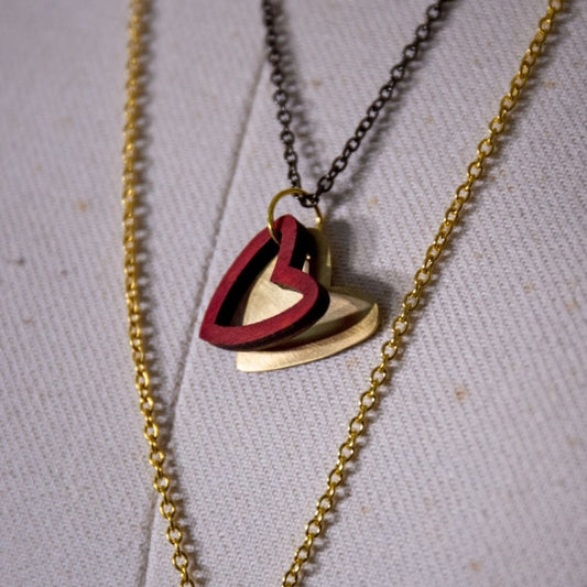 A necklace with a red wooden heart pendant layered over a gold-coloured hand-cut brass heart, hanging on an vintage style chain.